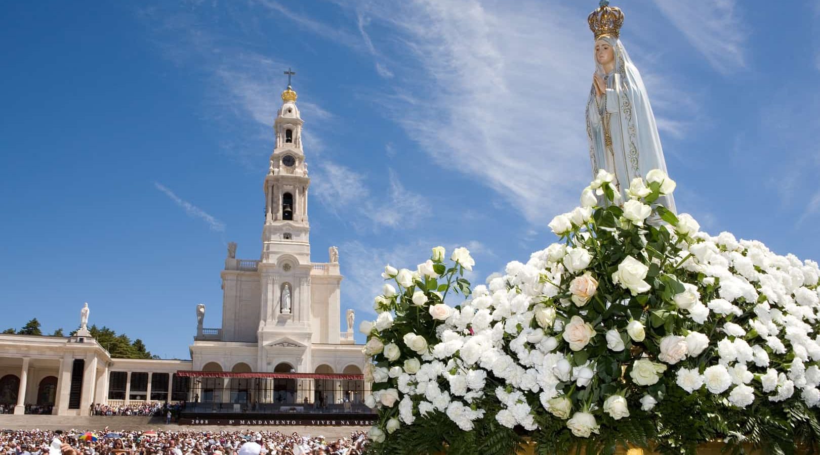 Statue of the Virgin Mary held by priests, surrounded by white roses and pilgrims at the Sanctuary of Fátima